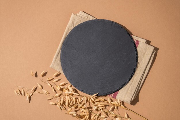 Black round slate empty board on a brown background with golden stalks of wheat and napkin