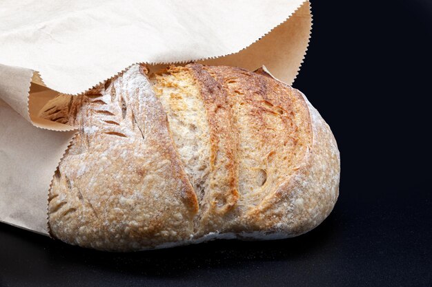 Black rye bread in flour and kraft paper bag on black background