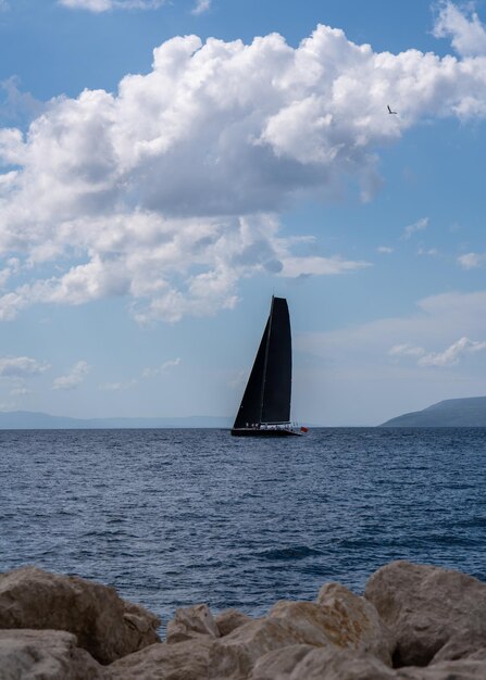 Черная парусная лодка с черными парусами в море Горы на горизонте активность на открытом воздухе в море