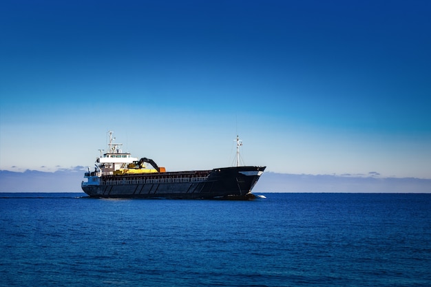 Черный парусный балкер. Грузовое судно с длинным вылетом экскаватора движется в стоячей воде в солнечный день у моря