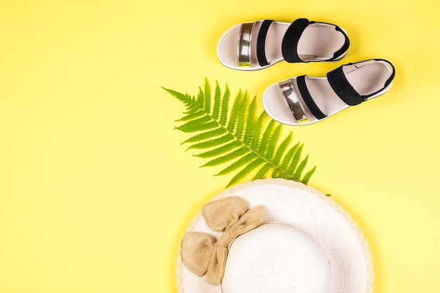 Black sandals a palm leaf and a hat on a yellow background