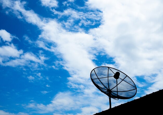 Black satellite TV receiver plate on the roof with a blue sky background