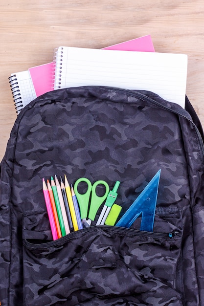 Black school bag with a set of stationery for the student and with white notebook in it. 