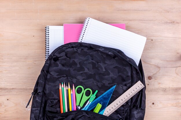 Black school bag with a set of stationery for the student and with white notebook in it. 