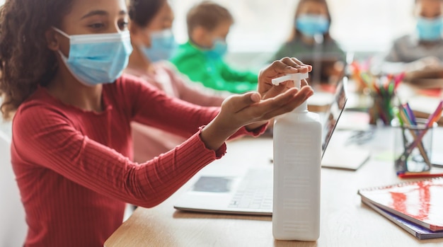 Foto studentessa nera che applica disinfettante disinfettante per le mani in classe a scuola