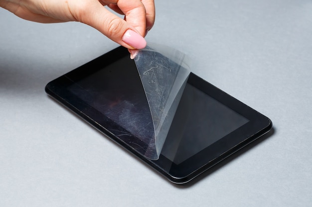 Black scratched tablet with a protective film on a gray background. Protect your device screen