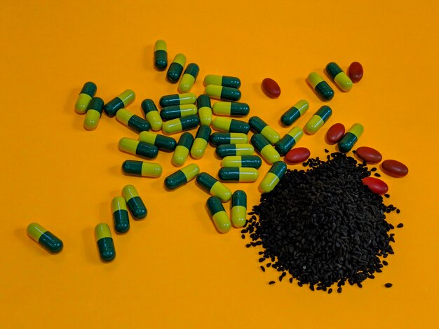 Black seeds and pills on orange background