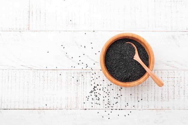 black sesame seeds in a bamboo bowl on white wooden surface. top view.