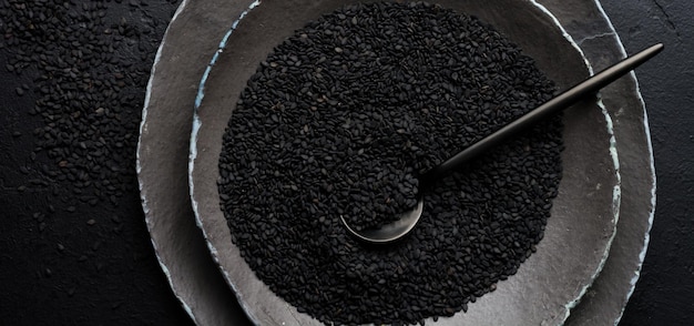 Black sesame seeds in black ceramic plates on a dark old vintage background. Rustic style. Top view