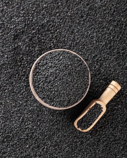 Black sesame seeds in a ceramic bowl and wooden spoon, selective focus, top view