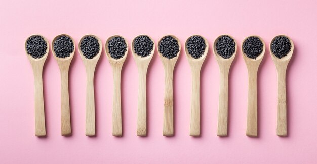 Black sesame seeds in wooden spoons on a pink background, top view