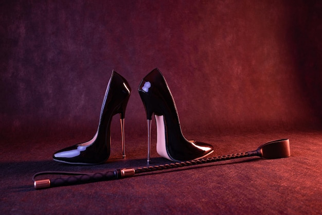 Black shiny high heel shoes and a whip on a dark background