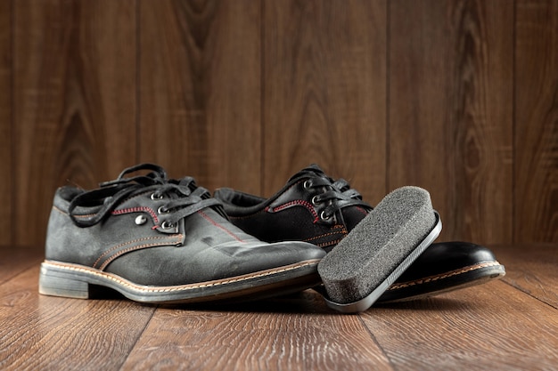 Black shoes one clean second dirty and brush on a wooden wall. The concept of shoe shine, clothing care, services.