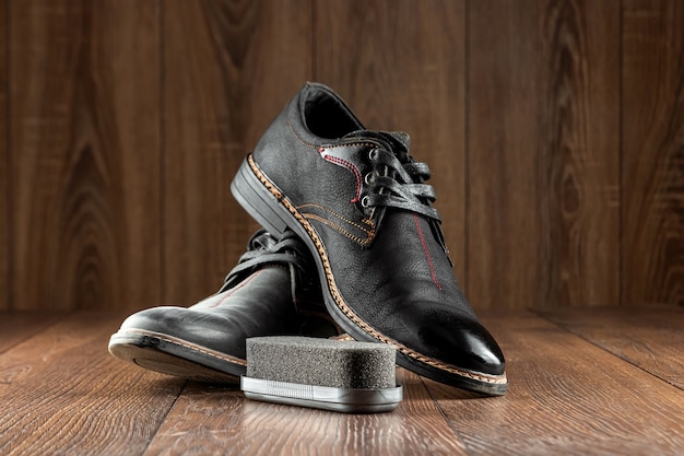 Черные ботинки одна чистая вторая грязная и щетка на деревянной стене. Концепция обуви, уход за одеждой, услуги.