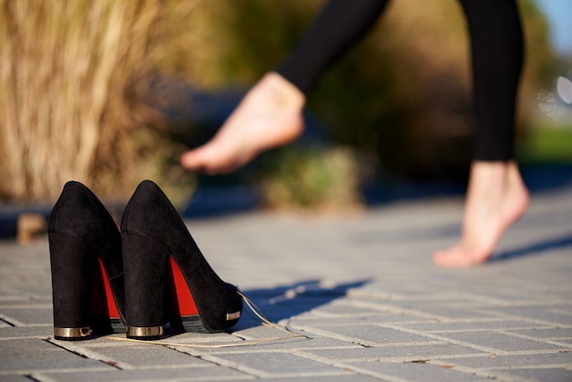 Scarpe nere sulla strada su uno sfondo gambe a piedi nudi femminili.