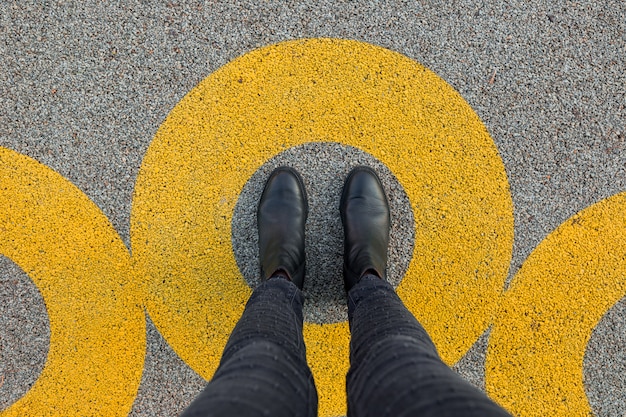 Black shoes standing in yellow circle on the asphalt concrete\
floor. comfort zone or frame concept. feet standing inside comfort\
zone circle