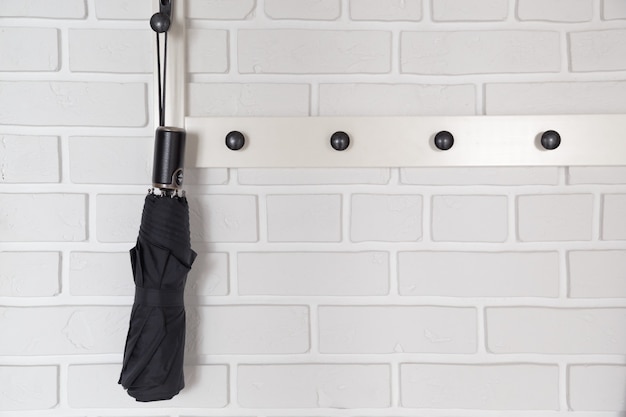 Black short umbrella hanging on hanger in white hallway interrior.