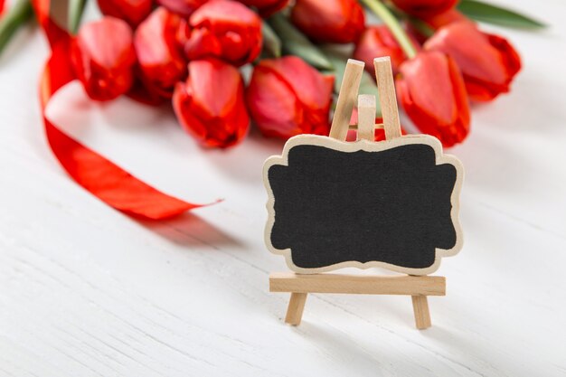 A black sign against a of red tulips on white table. The concept of Mother's Day. Copy space.