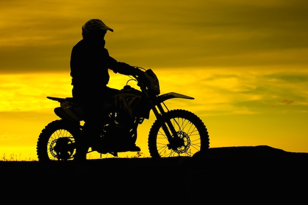 Black silhouette of biker with motobike on yellow sunset sky background