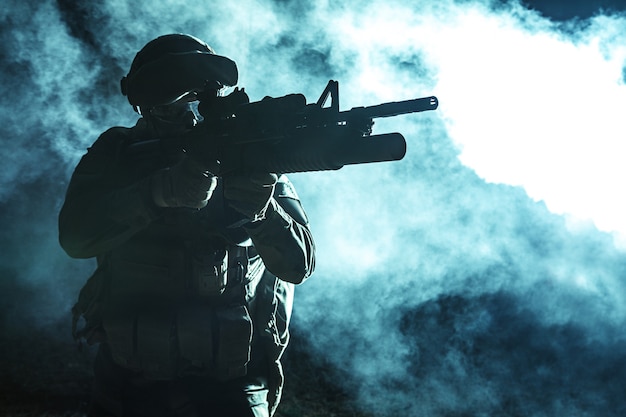 Photo black silhouette of soldier with grenade launcher in the smoke moving in battle operation. back light, cropped, toned and colorized