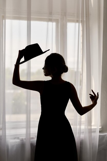 Black silhouette of a woman in a dress and hat at a window