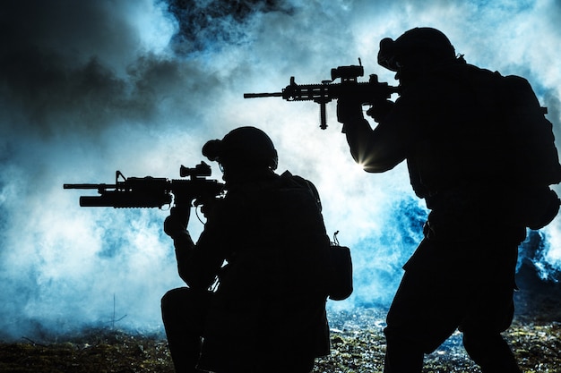 Black silhouettes of pair of soldiers in the smoke moving in battle operation. Back light