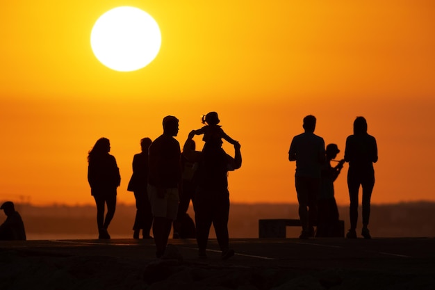 Black silhouettes of people walking on the hill at sunset