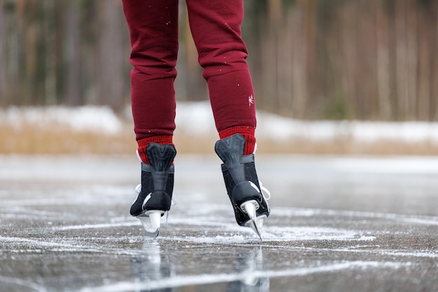 black skates on ice women's legs in burgundy pants stand on the surface of a frozen forest lake