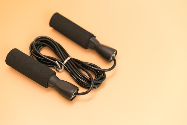 A black skipping rope lies down on the yellow background\
athletics effort gymnastic spirit endurance power weight leaping\
fit jumping sporting plastic object blue space element