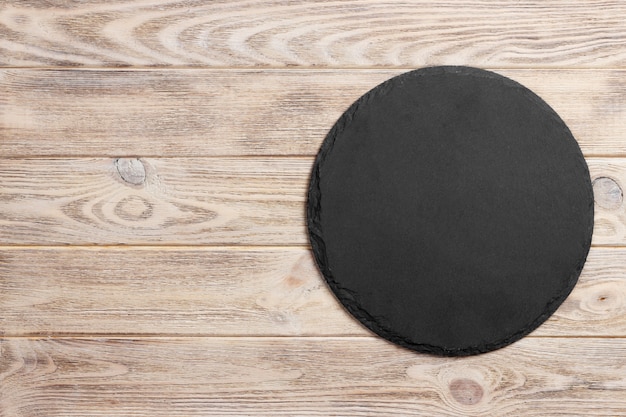 Black slate round stone on wooden surface, top view, copy space