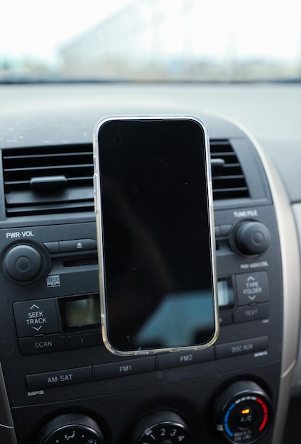 A black smart phone is on the dashboard of a car.