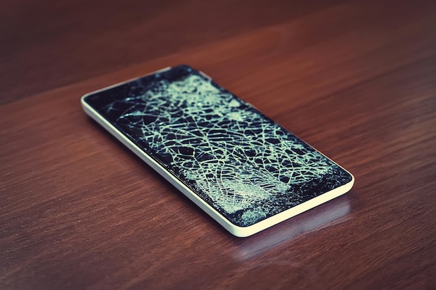 나무 테이블에 깨진 화면이 있는 검은색 스마트폰 전화 수리 개념 검은색 화면이 있는 오래된 깨진 전화기 디스플레이가 웹 형태로 금이 갔습니다.