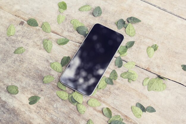 木のテーブルに葉が付いた黒いスマートフォン