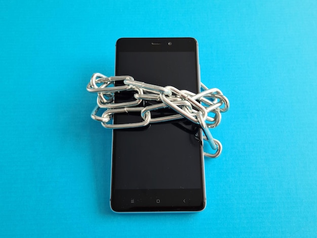 Black smartphone wrapped in metal chain closeup