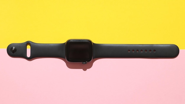 A black smartwatch lies on a colored background