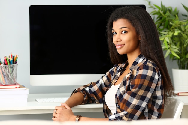 Black smiling woman sitting at workplace looking at camera