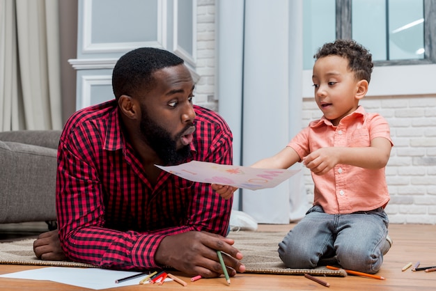 Black son showing drawing to amazed father 