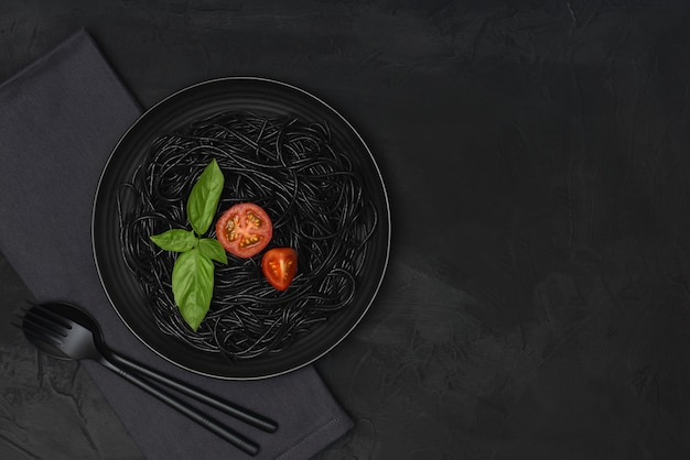 Black spaghetti with tomato and basil on black background with copy space. 