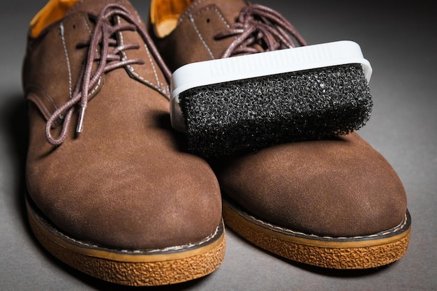 A black sponge for cleaning shoes lies on men\'s classic brown\
shoes with laces suede shoe care concept