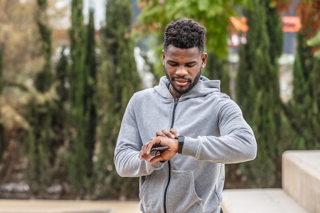 Black sportsman checking bracelet in park