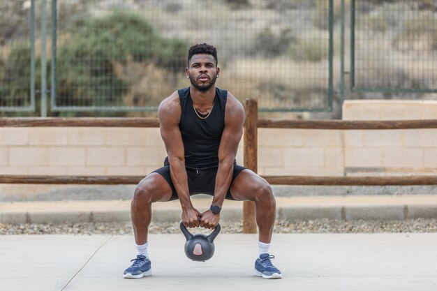 Black sportsman squatting with heavy weight during training