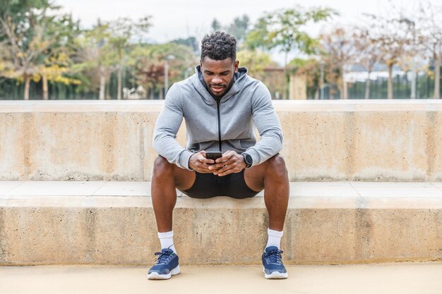 Black sportsman using smartphone on stairs