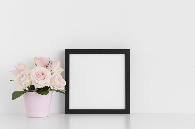 Black square frame mockup with pink roses in a pot on a white table