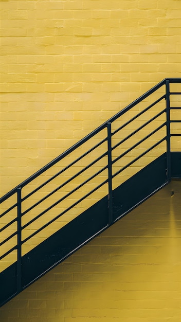 Photo black staircase on bright yellow background with diagonal handrail from top left to bottom right ver