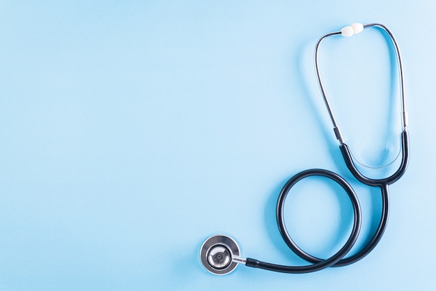 Black stethoscope on pastel blue table.