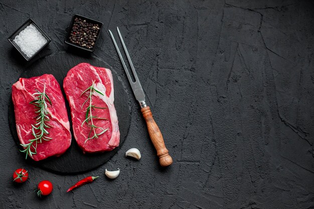 A black stone background with two raw steaks and a pair of garlic cloves.