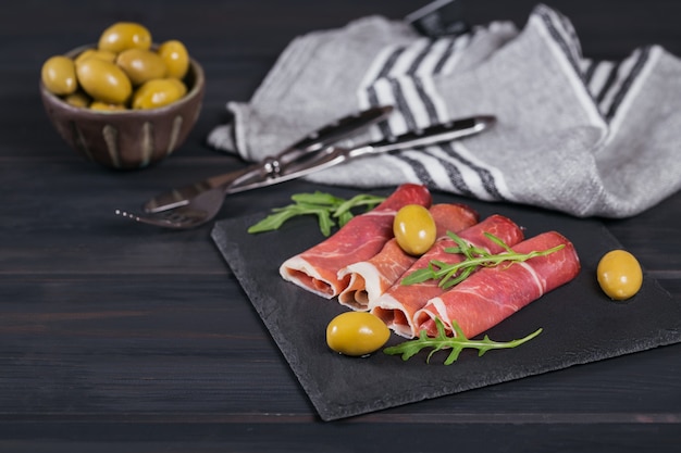 Black stone platter with slices of cured ham or Spanish jamon serrano or Italian prosciutto crudo