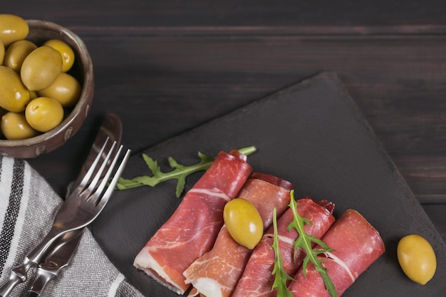 Black stone platter with slices of cured ham or Spanish jamon serrano or Italian prosciutto crudo