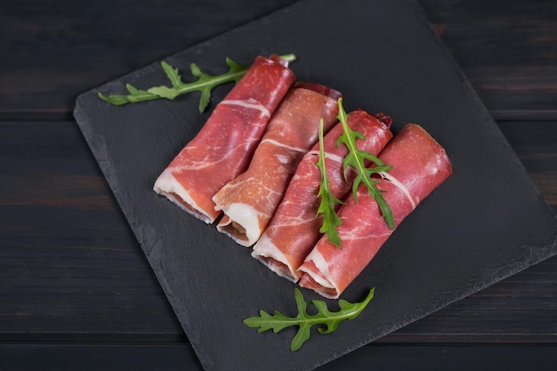 Black stone platter with slices of cured ham or Spanish jamon serrano or Italian prosciutto crudo