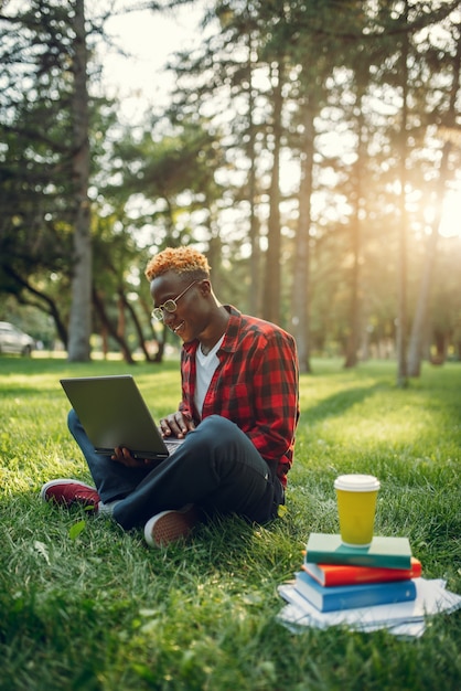 Photo black student with laptop sitting on the grass in summer park. a teenager studying and leisures outdoors